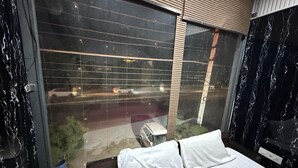 A hotel room with a large window, a bed with white bedding, and a view of the street outside. - Dream Lounge (Jalandhar)