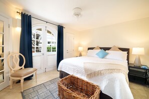 Ein Schlafzimmer mit einem Bett, einem Sessel, einem Korbwäsches und einem Nachttisch mit Lampe.