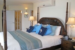 A neatly made bed with a wooden headboard, blue and white pillows, and a striped blanket. There are bedside lamps and a nightstand with a lamp and a shell. - Sapphire Beach 201 3 Bedroom Apts (St. Lawrence Gap)