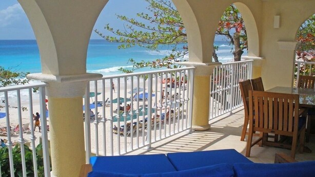 Ein Balkon mit Blick auf Strand und Meer, mit weißen Geländern und blauer Sitzgelegenheit.