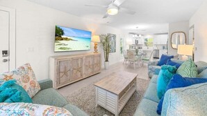 Ein Wohnzimmer mit Fernseher, Deckenventilator, Essbereich und einer Küche im Hintergrund.