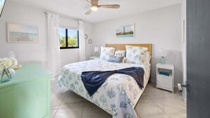 Ein Schlafzimmer mit Bett, Nachttisch, Kommode, Deckenventilator und einem Fenster mit Vorhängen.