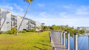 Ein modernes Hotel mit Glasfassade, einer Rasenfläche, einer Palme und Blick auf das Wasser.