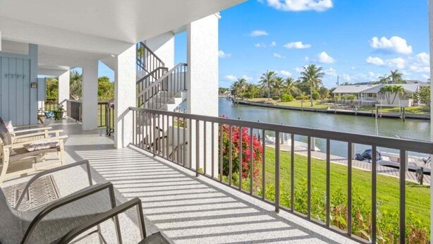 Ein Balkon mit Sitzgelegenheit, eine Treppe und Blick auf Wasser und Grünflächen.