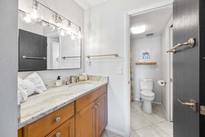 A bathroom with a marble vanity, a large mirror with lights, a towel rack, and a toilet. - Tennis Place Unit B22 2 Bedroom Condo (Sanibel)