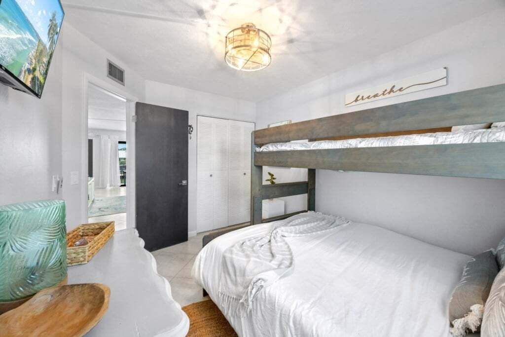 Un dormitorio con literas, una mesita de noche, una lámpara y un televisor instalado en la pared.