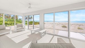 A spacious room with large windows overlooking a beach, a ceiling fan, and a white sofa. - Sandy Bend 2 2 Bedroom Condo (Sanibel)