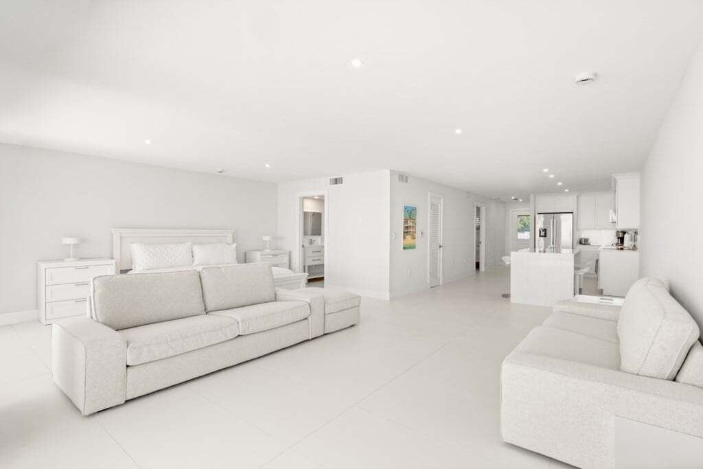 Un saló modern amb temàtica blanca, amb un sofà, una taula de centre i una zona de cuina al fons.