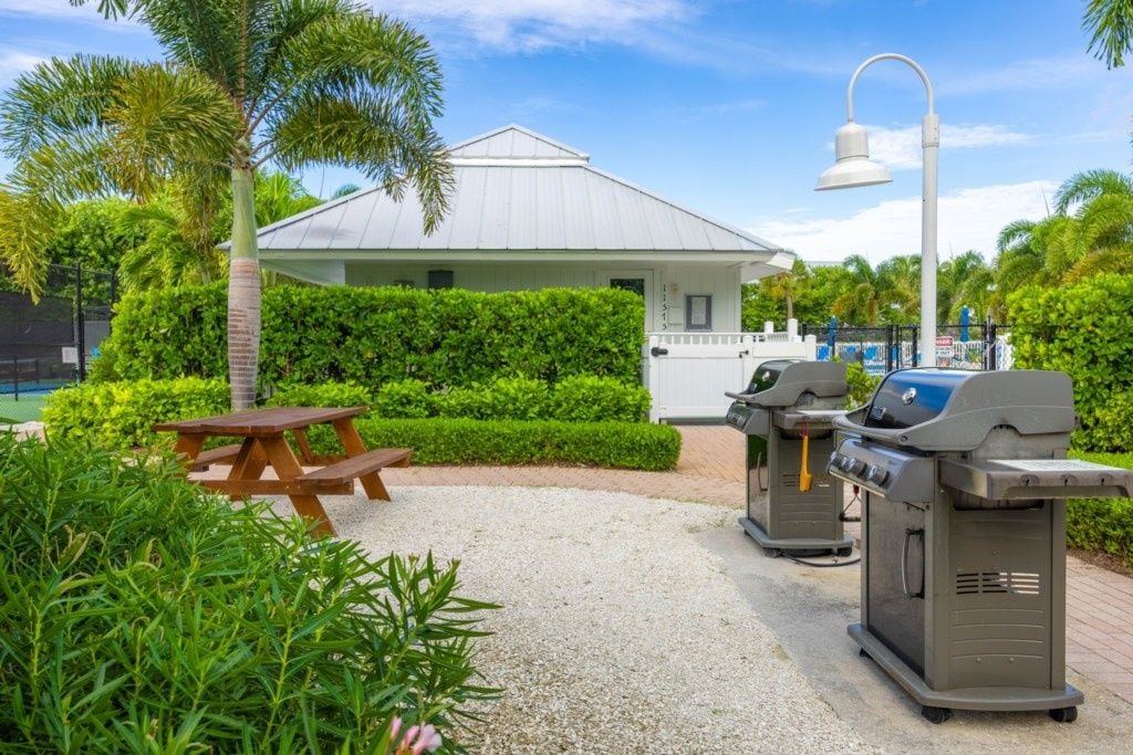 Un área de patio con una estación de parrilla, una mesa de picnic y un pequeño edificio con techo blanco.