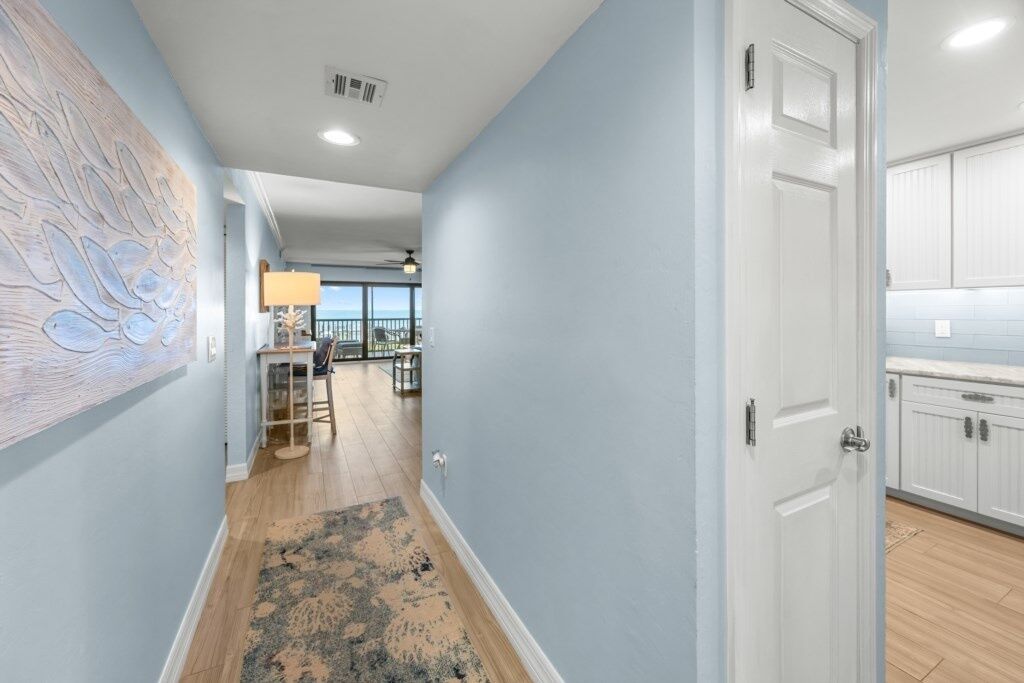 A hallway with a wooden floor, a rug, and a door leading to a kitchen with white cabinets.