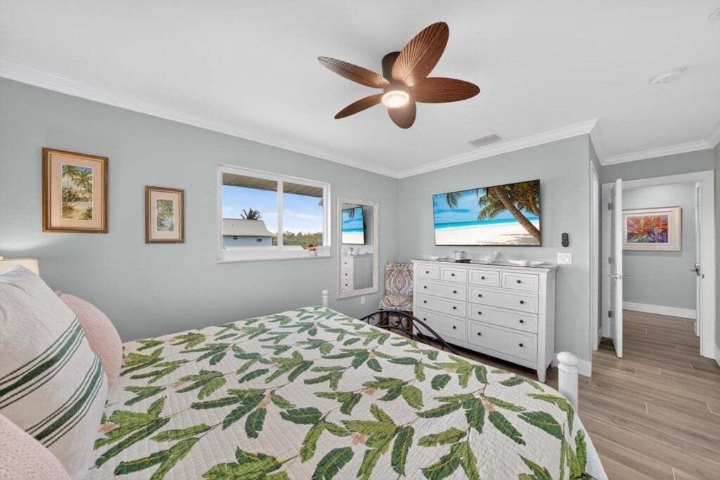 Un dormitorio con cama, cómoda, ventilador de techo y ventana con vista a la playa.