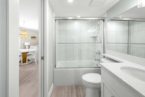A modern bathroom with a glass-enclosed shower, a white toilet, and a large mirror above the sink. - Sandy Bend 8 2 Bedroom Condo (Sanibel)
