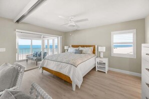 A bedroom with a bed, a nightstand, a chair, a ceiling fan, and a view of the ocean through a sliding door. - Sandy Bend 8 2 Bedroom Condo (Sanibel)