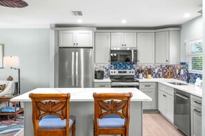 A modern kitchen with grey cabinets, stainless steel appliances, and a tiled backsplash. - Seashells Unit 06 2 Bedroom Condo (Sanibel)