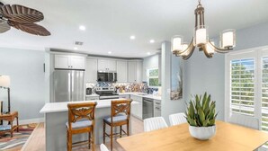 A modern kitchen with white cabinets, stainless steel appliances, and a wooden dining table with chairs. - Seashells Unit 06 2 Bedroom Condo (Sanibel)