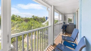 A balcony with two chairs, a small table, and a view of greenery and buildings. - Seashells Unit 06 2 Bedroom Condo (Sanibel)