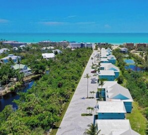 A row of blue-roofed buildings along a waterfront, surrounded by greenery and a small body of water. - Seashells Unit 19- Sanibel Sunset 2 Bedroom Condo (Sanibel)