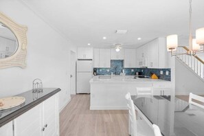 A modern kitchen with white cabinetry, a central island, and a blue backsplash. - Seashells Unit 19- Sanibel Sunset 2 Bedroom Condo (Sanibel)