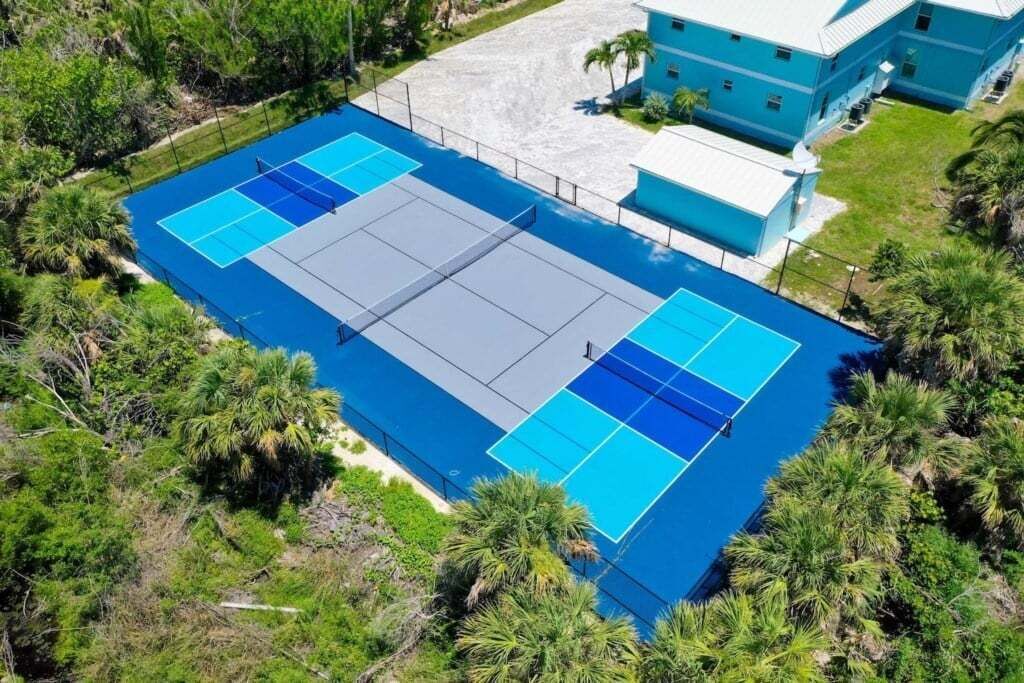 En vy från ovan av en tennisbana omgiven av frodig grönska och en byggnad med ett blått tak.
