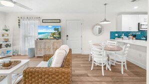 Ein modernes Wohnzimmer mit Fernseher, weißen Möbeln und einer Küchenzeile mit blauen Fliesen.