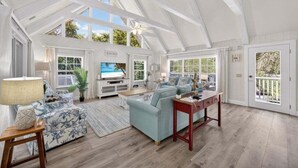 A spacious living room with a high ceiling, large windows, and a television.