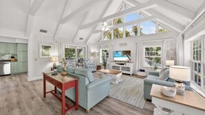 A spacious living area with a high ceiling, large windows, and a view of the outdoors.