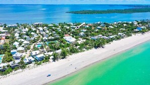 An aerial view of a coastal resort with beachfront properties, clear blue waters, and a small island in the distance.