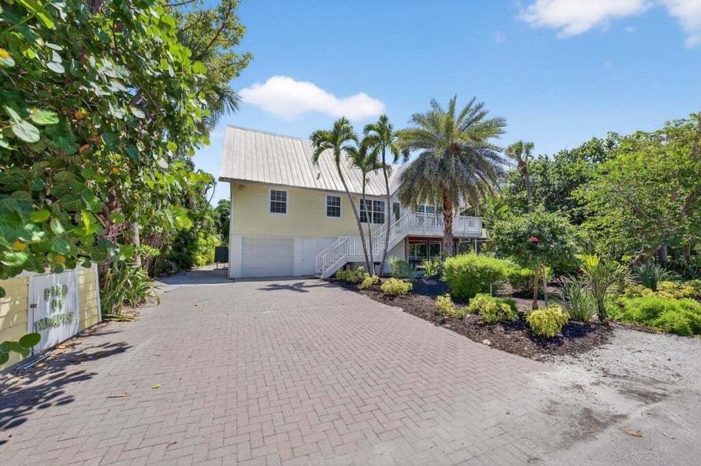 A two-story building with a paved driveway and a small garden with palm trees and shrubs.
