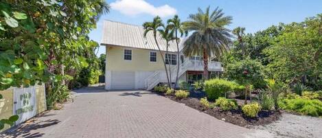 A two-story building with a paved driveway and a small garden with palm trees and shrubs.