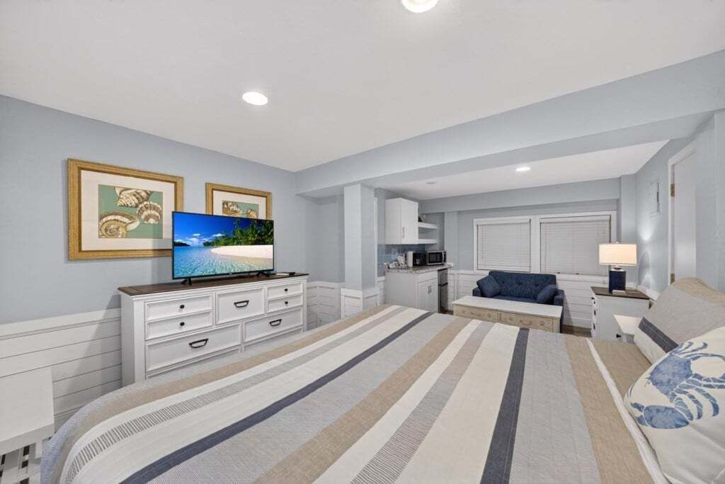 A bedroom with a large bed, a TV, a sofa, and a desk with a lamp.