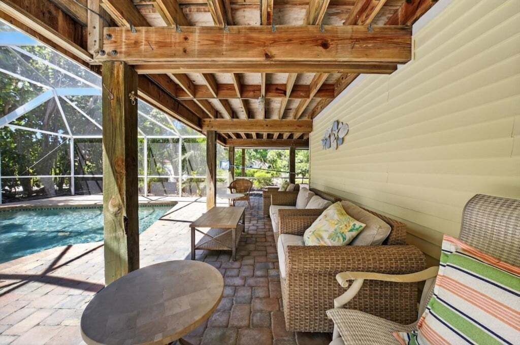 An outdoor patio area with a pool, wicker furniture, and a wooden ceiling structure.