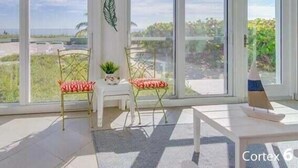 Ett ljust rum med stora fönster, vita möbler och utsikt över grönområden utanför.