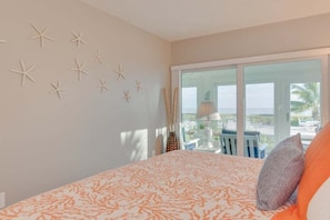 A bedroom with a large bed, starfish wall decor, a view of the outdoors, and a balcony with a table and chairs. - Sandy Bend 3 2 Bedroom Condo (Sanibel)