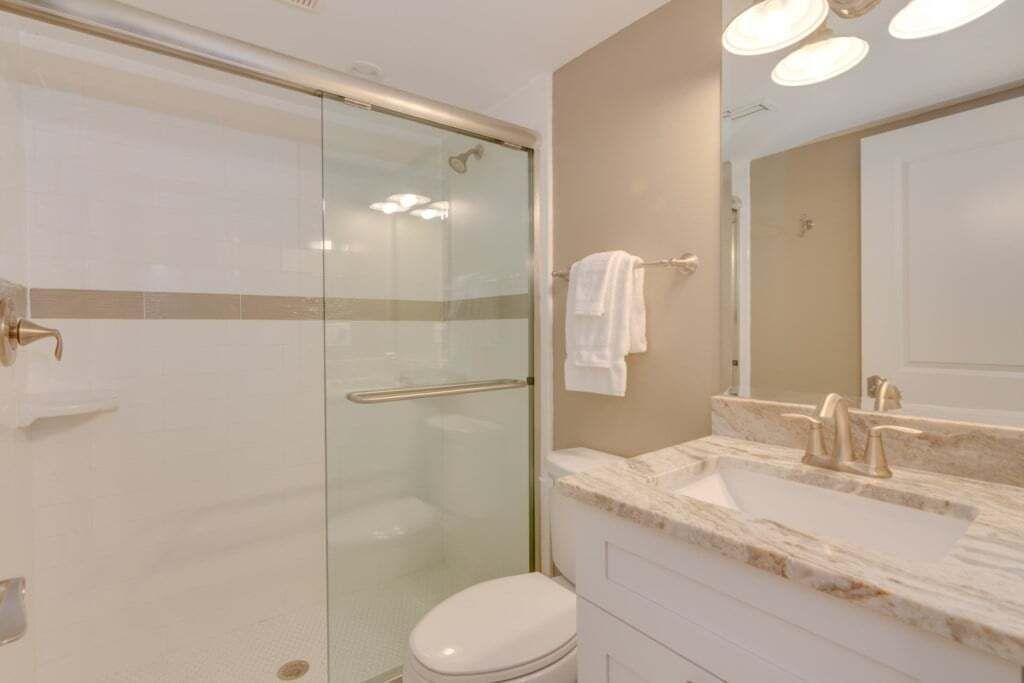 A modern bathroom with a glass-enclosed shower, a white toilet, and a marble sink with a large mirror.