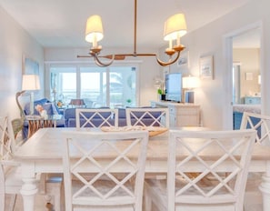 A dining area with a white table and chairs, a chandelier, and a view of the outdoors. - Sandy Bend 3 2 Bedroom Condo (Sanibel)