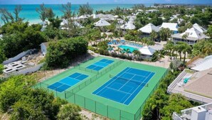Un resort con varias canchas de tenis, piscina y vista al océano.