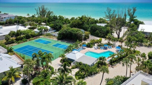 Un resort con cancha de tenis, piscina y vistas a la playa.