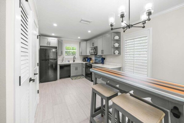 A modern kitchen with white cabinets, a stainless steel refrigerator, and a bar area with stools. - Seashells Unit 24 2 Bedroom Condo (Sanibel)