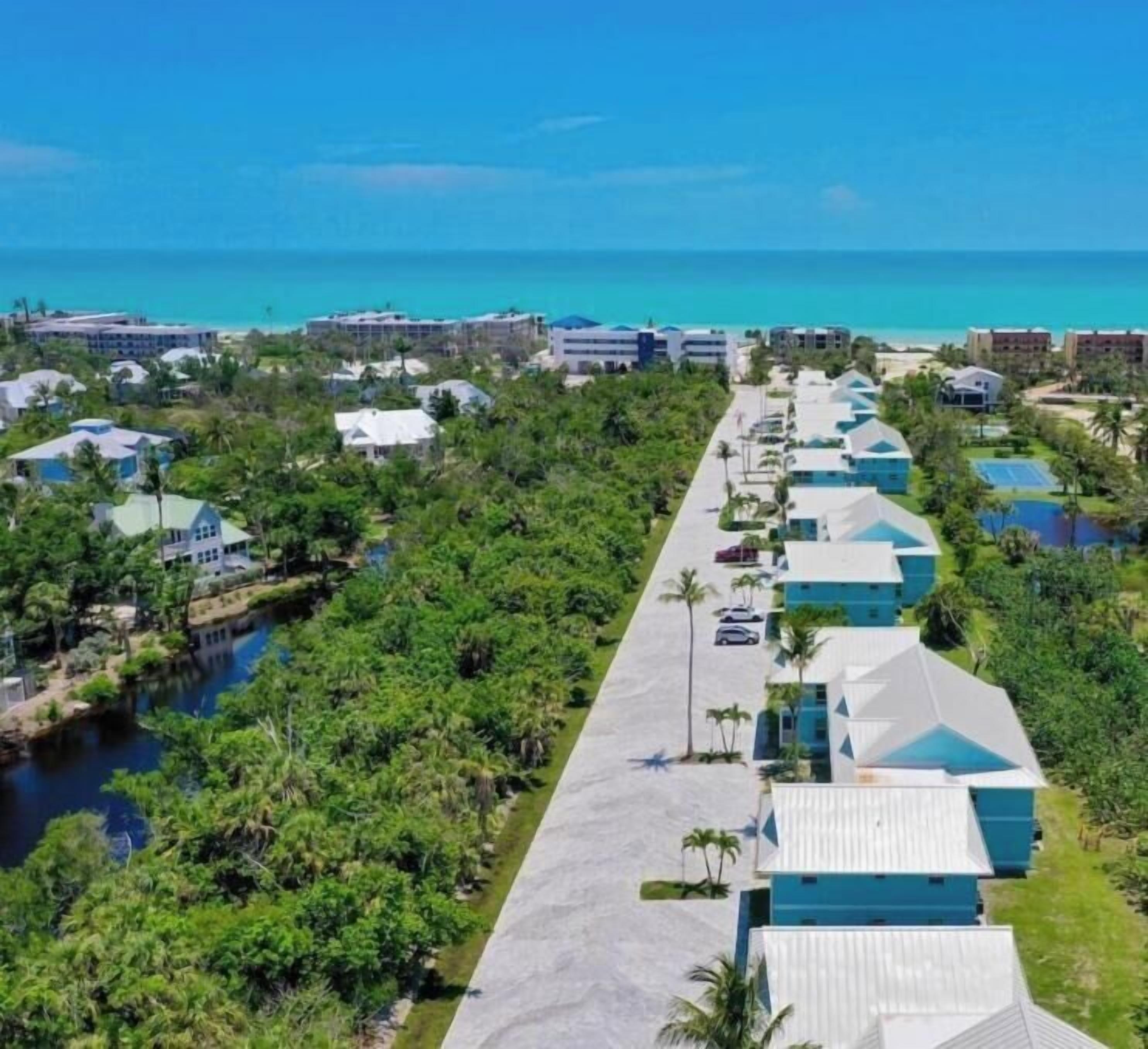Ein Resort mit mehreren Bungalows, die entlang eines zentralen Weges angeordnet sind, mit einer Wasserfläche auf der einen Seite und einem Strand in der Ferne.