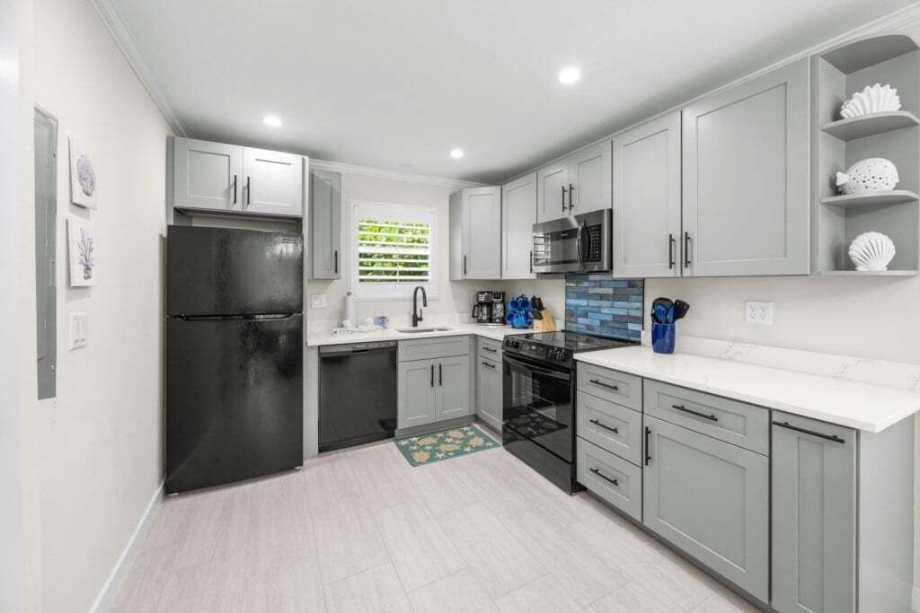 A modern kitchen with grey cabinets, a black refrigerator, a microwave, and a sink.