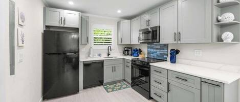 A modern kitchen with grey cabinets, a black refrigerator, a microwave, and a sink.