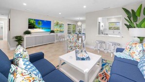 Uma sala de estar moderna com um sofá, mesa de centro e uma TV exibindo uma cena de praia.