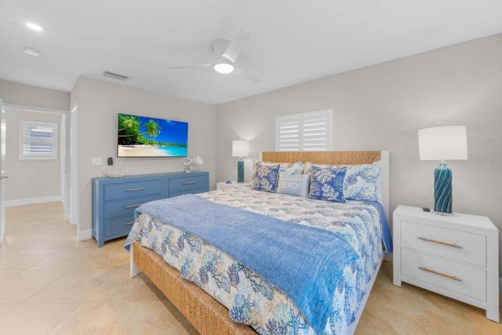 A bedroom with a bed, a dresser, a nightstand, a ceiling fan, and a TV on the wall.
