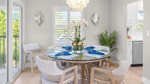 Uma sala de jantar com uma mesa de vidro, cadeiras de vime, um candelabro e vista para o exterior.