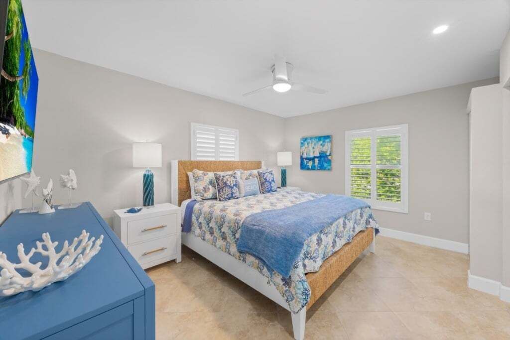 A bedroom with a bed, nightstands, a dresser, a ceiling fan, and a window with blinds.