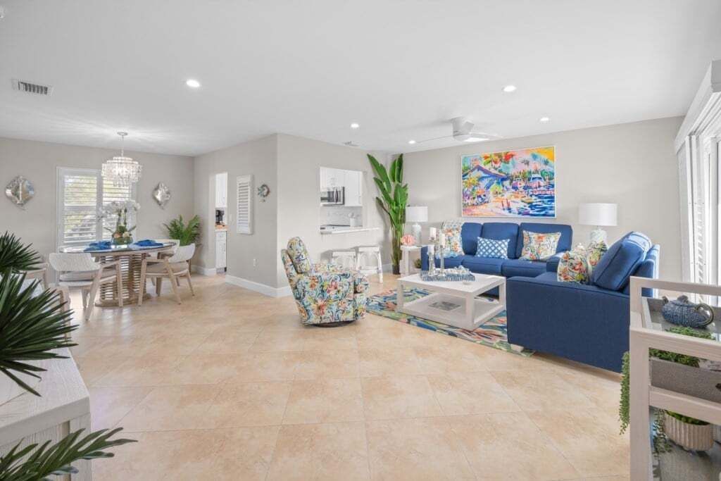 A spacious living room with a blue sofa, a dining area with a white table, and a kitchen area in the background.