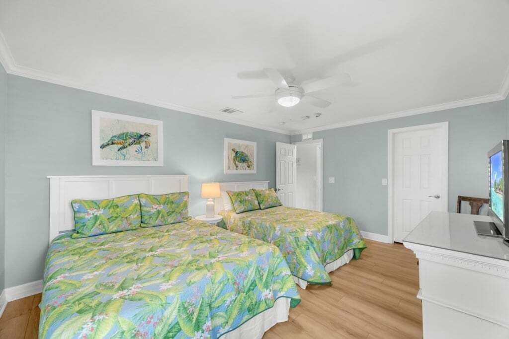 Een slaapkamer met twee bedden, een plafondventilator en kunstwerken aan de wanden.