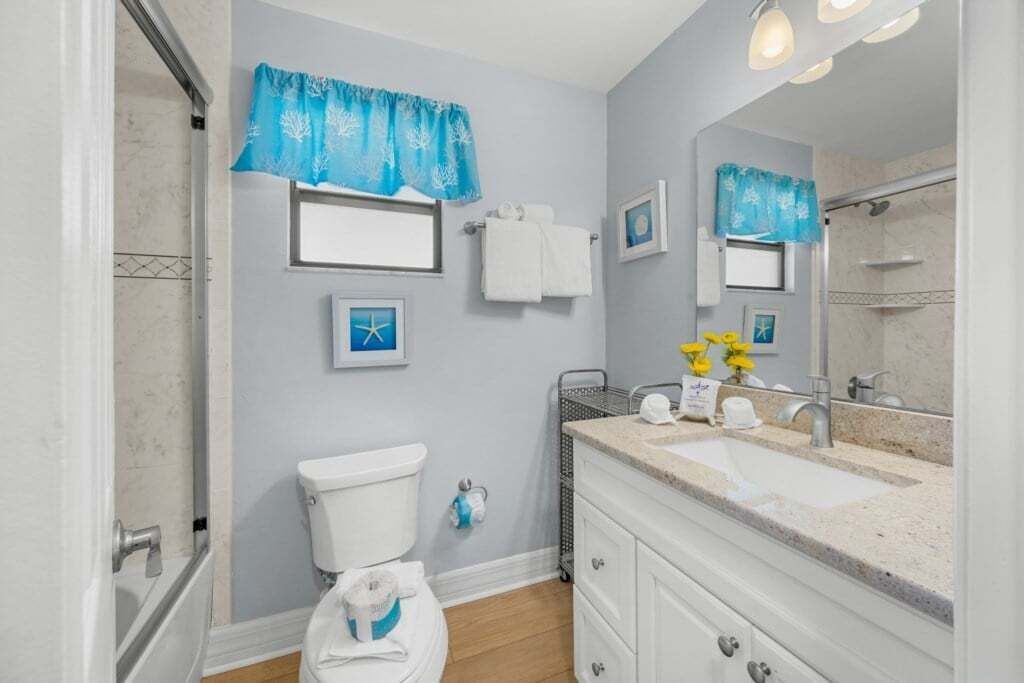 A bathroom with a toilet, sink, and shower. There are towels and a basket on the counter.