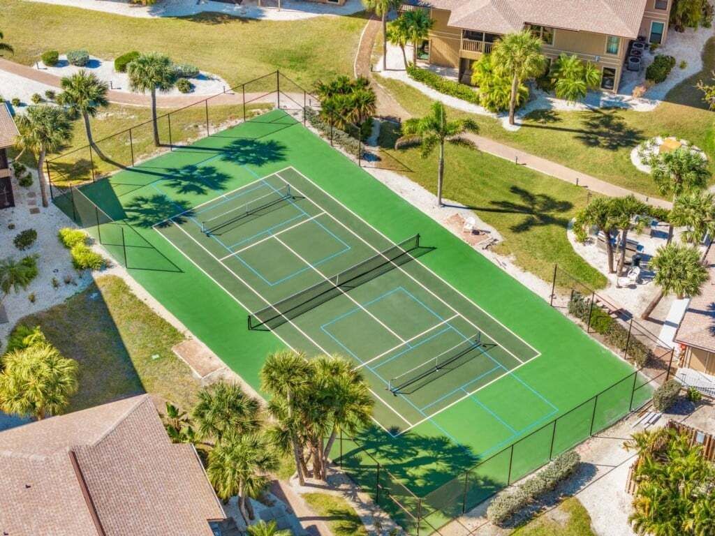 An aerial view of a tennis court surrounded by palm trees and residential buildings.