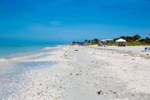 Una playa con arena blanca, agua azul cristalina y algunas sombrillas y sillas de playa.